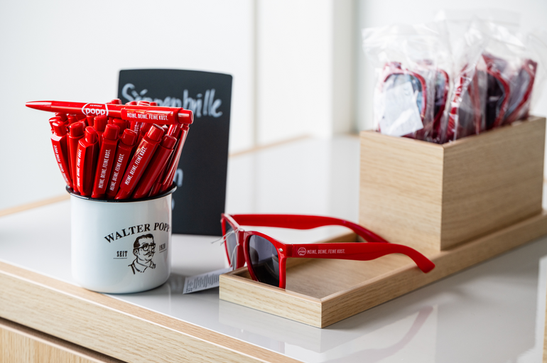 Mehrere rote Kugelschreiber in einer Tasse, deneben eine Sonnenbrille.