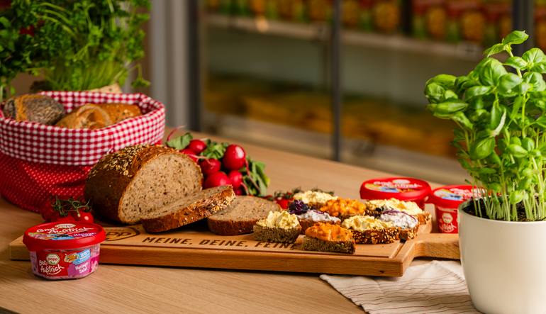 Ein aufgeschnittenes Mehrkornbrot, welches auf einem Brett liegt. Daneben liegen verschiedene geschmierte Brote und verpackte Produkte.